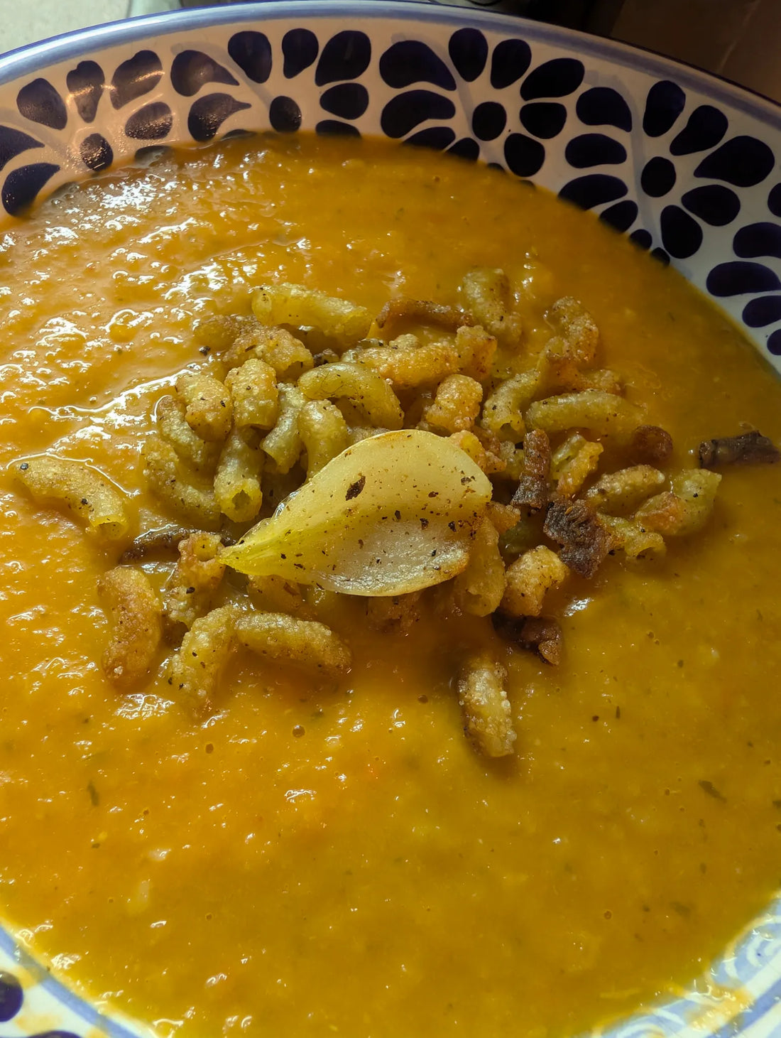 Bol de soupe aux lentilles rouges garnie de croustilles et d’ail noir, préparée avec les Épices du Pharaon et du sel Umami de la Montagne.